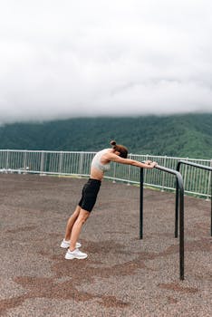 Woman stretching on a railing outdoors with a scenic mountain background, promoting healthy lifestyle.