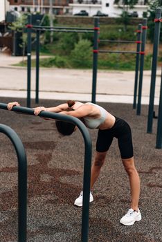Woman stretching by railing in an outdoor fitness park, promoting a healthy lifestyle.