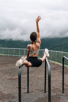 Woman in activewear performing splits on outdoor bars with a mountain backdrop.