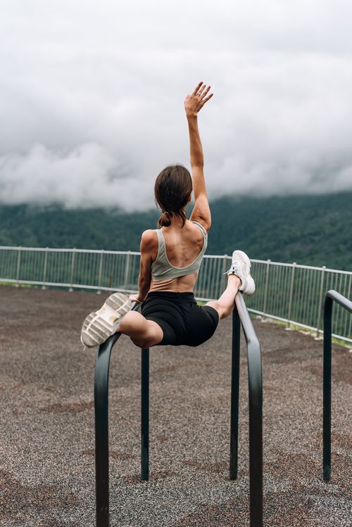 Free Woman in activewear performing splits on outdoor bars with a mountain backdrop. Stock Photo