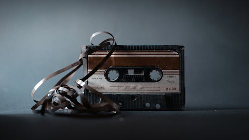 Retro audio cassette with tape out placed on gray surface and illuminated by light in studio