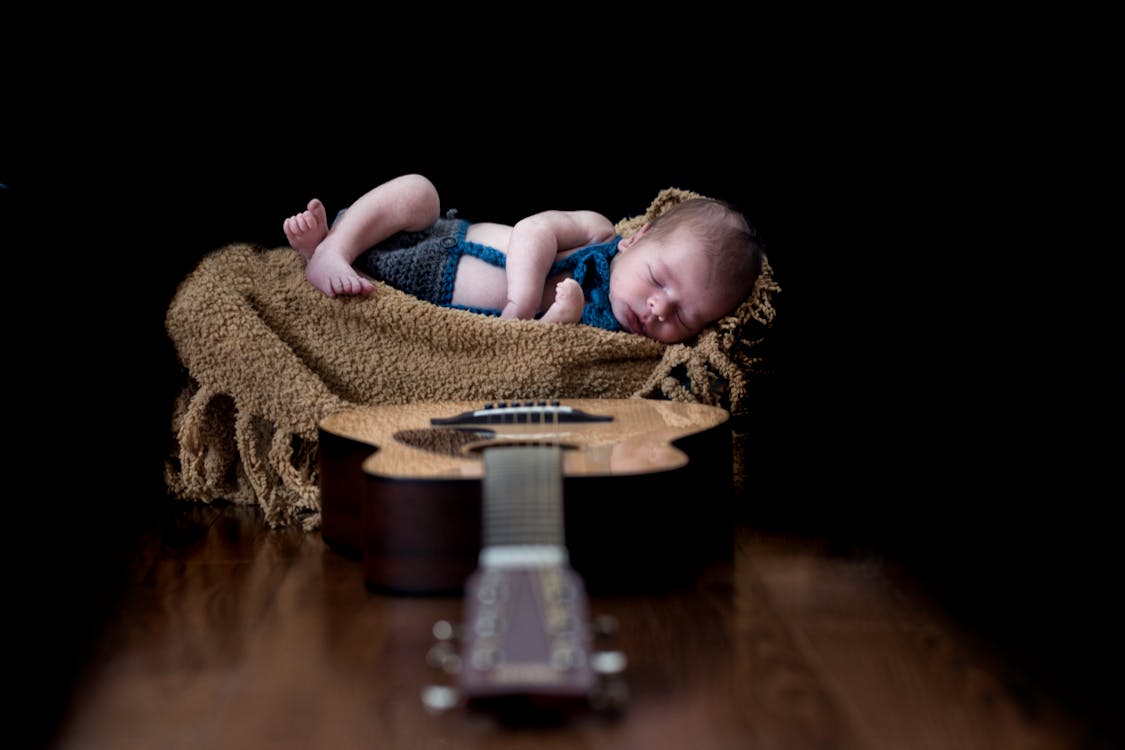 Ребенок на бежевой ткани возле коричневой акустической гитары дредноут