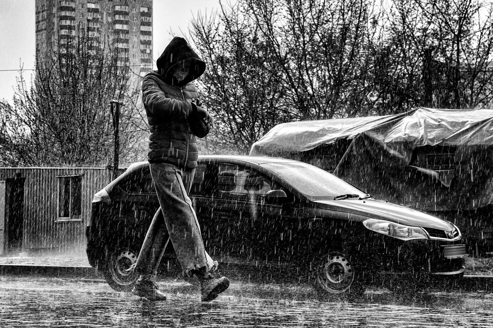Uomo con giacca con cappuccio che cammina sotto la pioggia in città