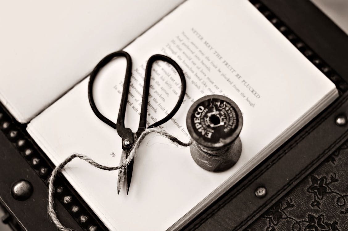 Free Black Scissors Near Thread Reel on White Book Page Stock Photo