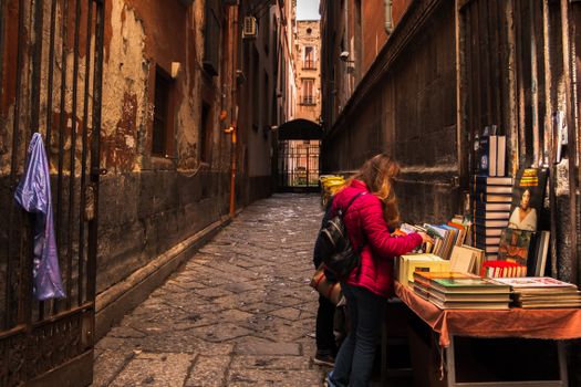 Side view of anonymous female shopper and child picking textbook at table with assorted literature in town