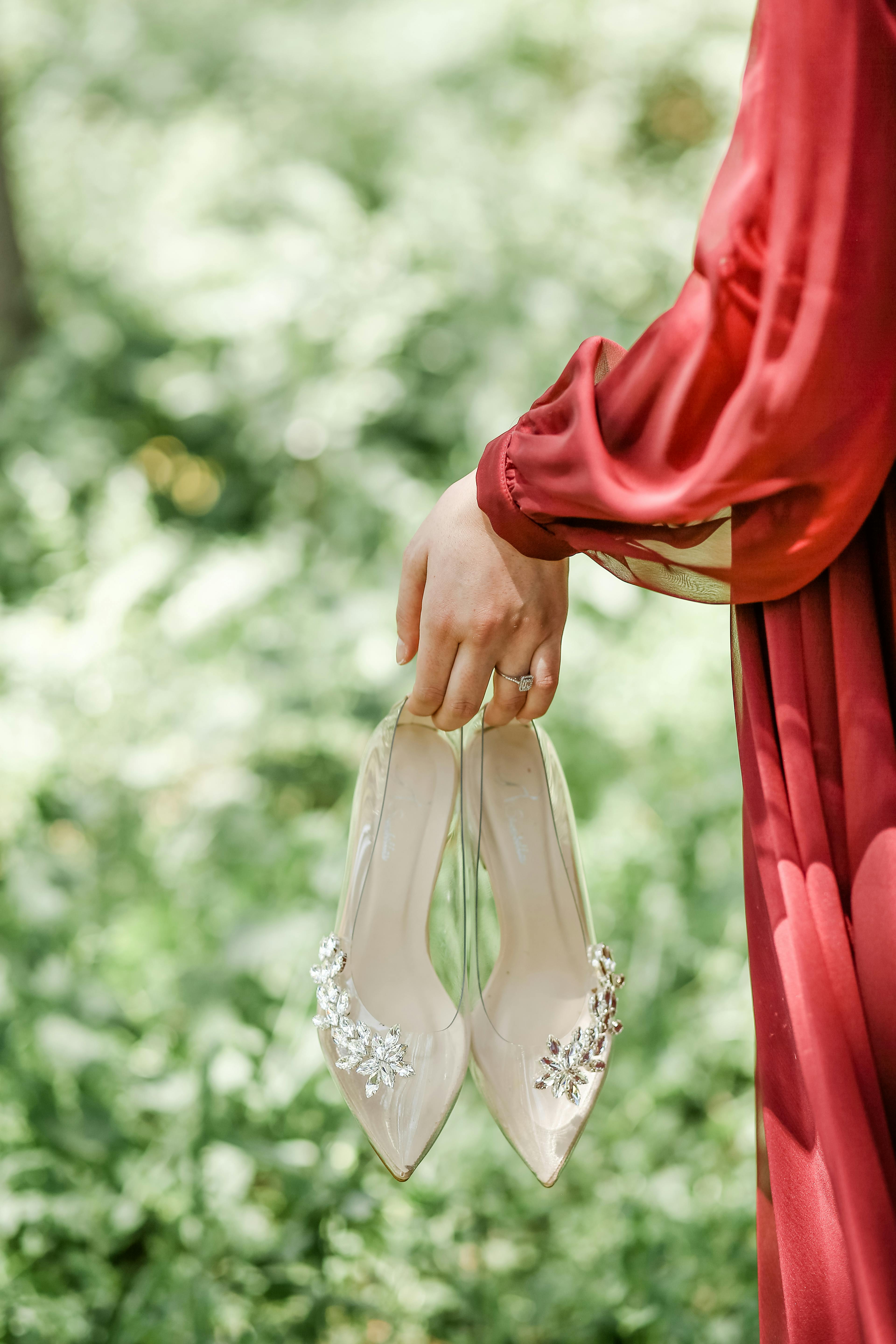 Close-up of a woman holding crystal embellished shoes in a garden setting, conveying elegance and style.