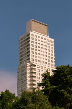 Tall high-rise building against a clear blue sky with green trees at the base.