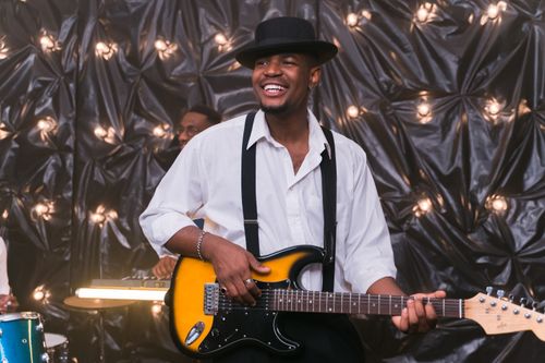 Free Smiling musician in hat playing electric guitar at a festive indoor concert. Stock Photo