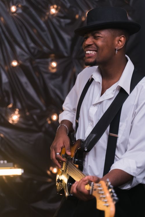 Free Smiling male guitarist in hat plays electric guitar enthusiastically indoors. Stock Photo