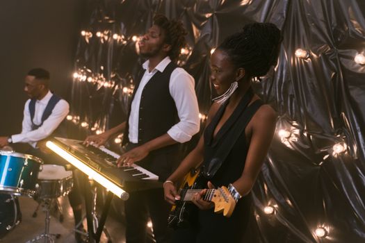 Vibrant indoor band performance featuring a guitarist, pianist, and drummer playing together.