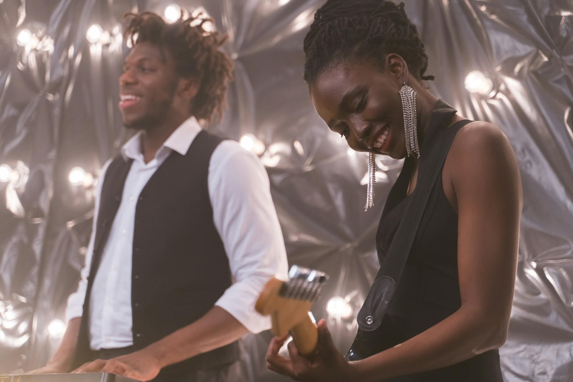 Smiling musicians playing guitar and piano during a lively indoor performance.