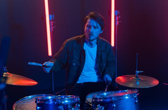 A male drummer energetically playing drums under vibrant stage lighting.