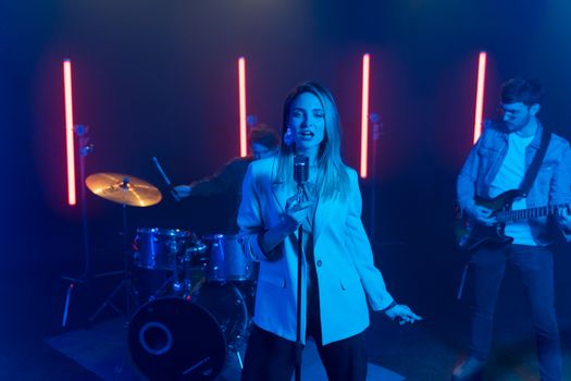 A vibrant live band performance featuring a female vocalist, drummer, and guitarist.