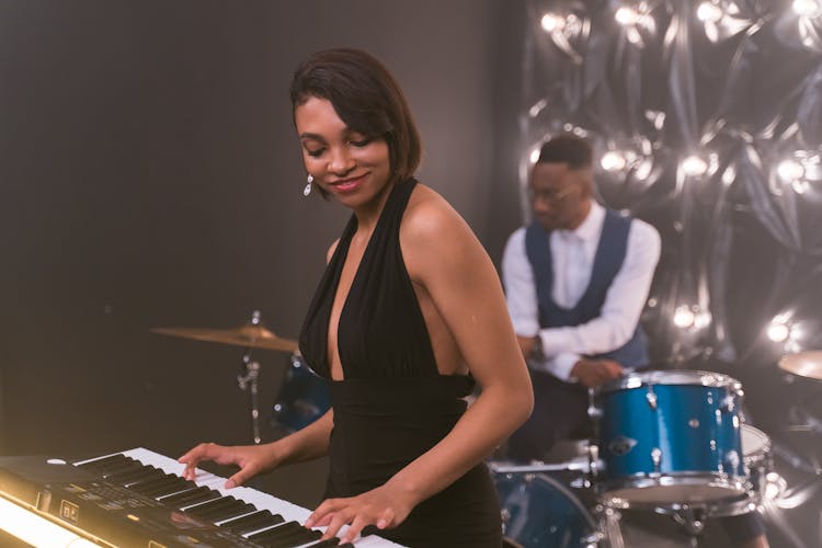 Woman Playing A Keyboard And A Man Playing The Drums In The Back 