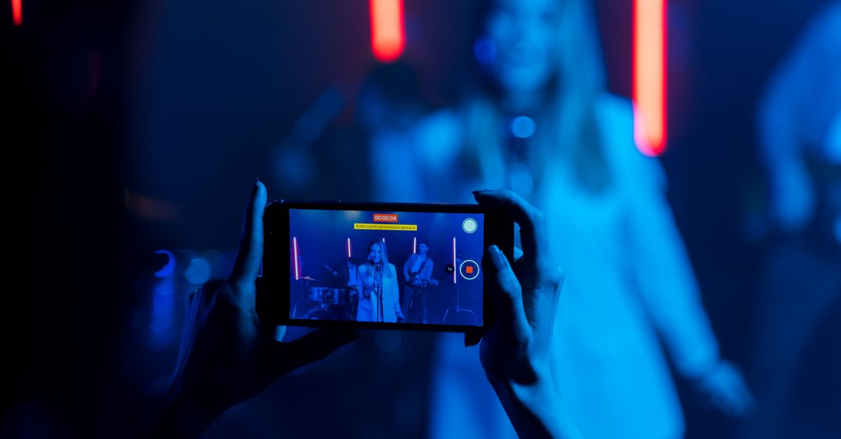 Spotify launches first global music video chart alongside expanded artist tools and video uploads A woman recording a live music performance with vibrant neon lights using her smartphone.