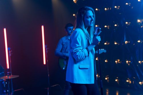 Free A female vocalist performs on stage with a band, illuminated by colorful lights. Stock Photo