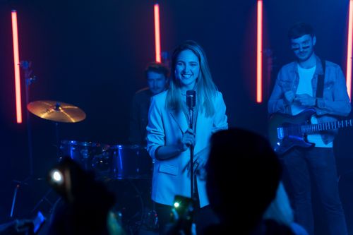 Free Energetic live performance with a band on stage, featuring a smiling singer with guitar and drums. Stock Photo