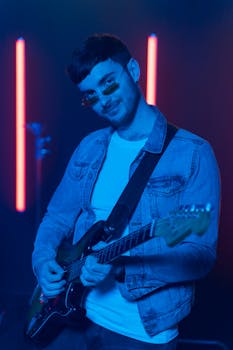A stylish guitarist in a denim jacket performs under colorful stage lights, capturing the essence of live music.