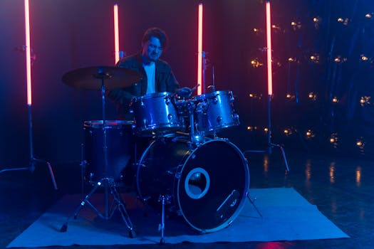 Musician playing drums on stage, surrounded by vibrant neon lights.
