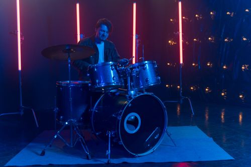 Free Musician playing drums on stage, surrounded by vibrant neon lights. Stock Photo