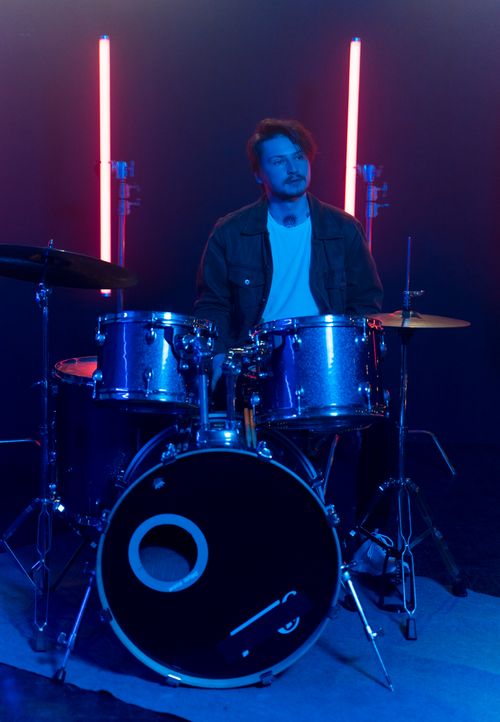 Free Young musician in black jacket playing drums with neon lights backdrop. Stock Photo