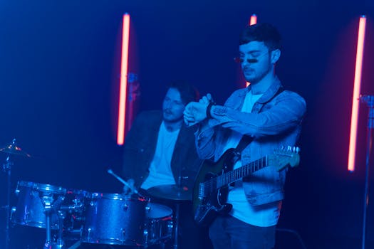 Musicians playing guitar and drums on a neon-lit stage, creating an electric atmosphere.