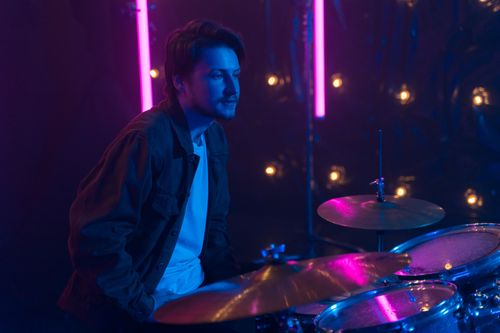 Free Male drummer in a denim jacket performing under vibrant neon lighting. Stock Photo
