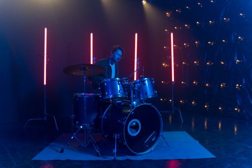 Free A musician plays drums under dramatic neon lights in a dark studio setting. Stock Photo