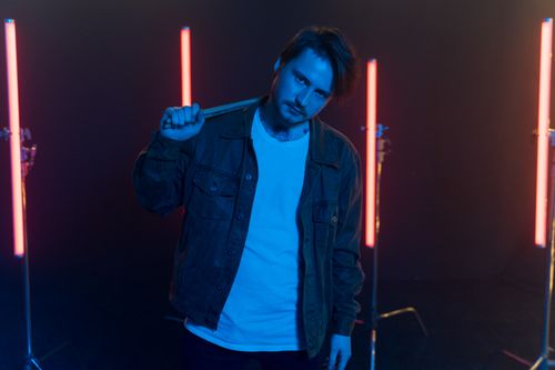 Free A young male drummer poses with neon lights in a dark studio setting, creating a vibrant atmosphere. Stock Photo