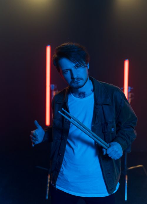 Free Portrait of a man holding drumsticks in a moody studio setting with neon lights. Stock Photo