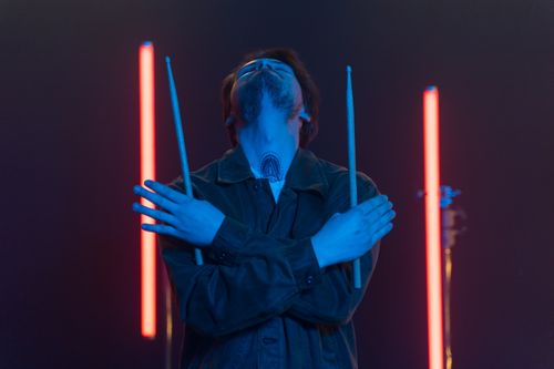Free A man dramatically poses with drumsticks crossed under neon lights, conveying artistic expression. Stock Photo