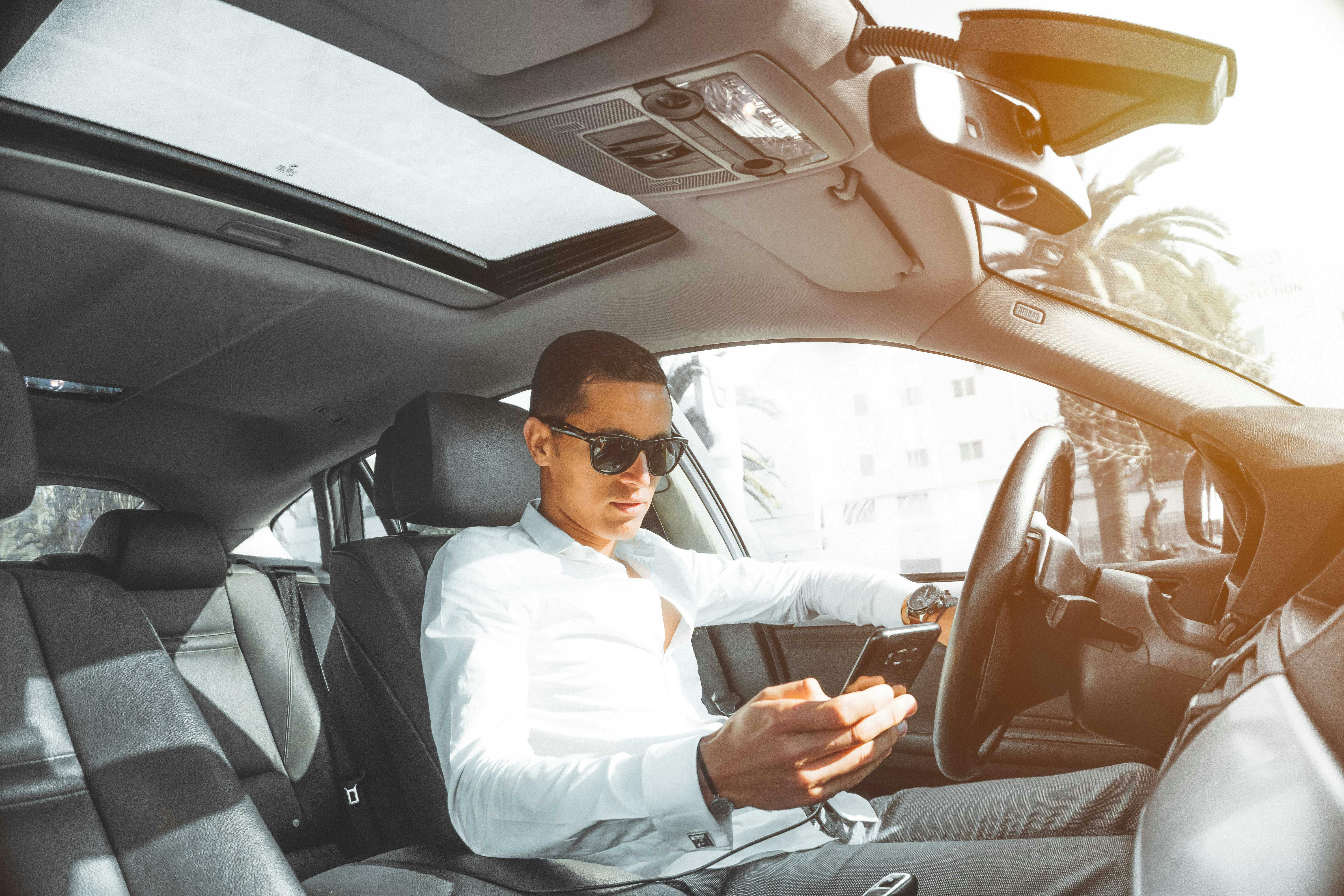 Inside the car, a man holds his smartphone. | Photo: Pexels