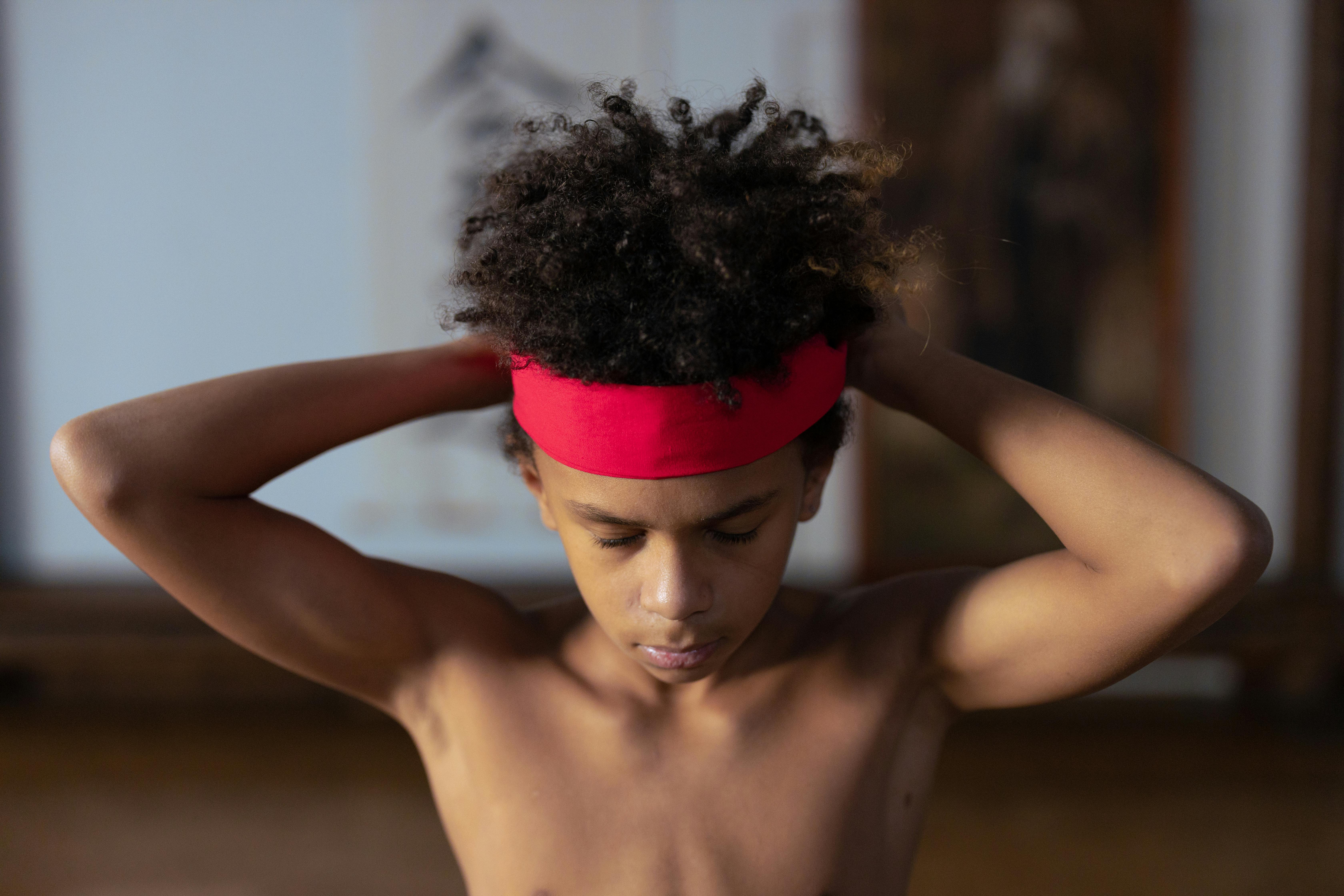 Close-up of a young boy in a red headband focusing before martial arts practice indoors.