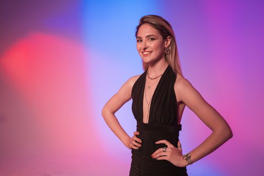 Smiling woman in a stylish black dress with jewelry in vibrant studio lighting.