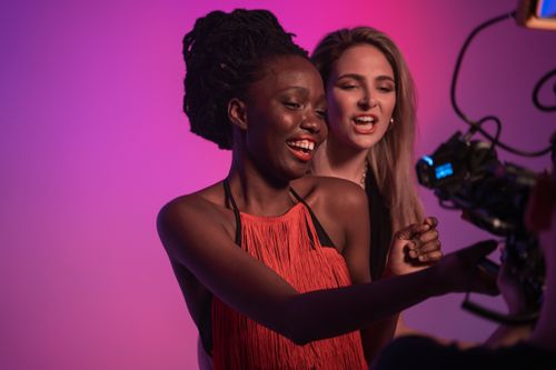 Free Two women enjoying a fashionable photoshoot in a studio setting with vibrant lighting. Stock Photo