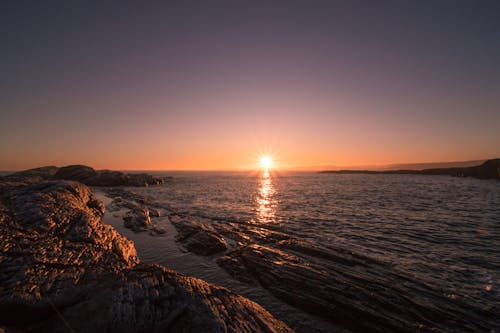 Brown Rocks Beside Body of Water during Sunset