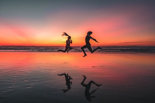 Silhouette of Man and Woman Jumping on Beach during Sunset 