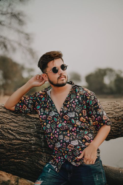 Free Fashionable man in casual wear leaning on a tree outdoors in Delhi, India. Stock Photo