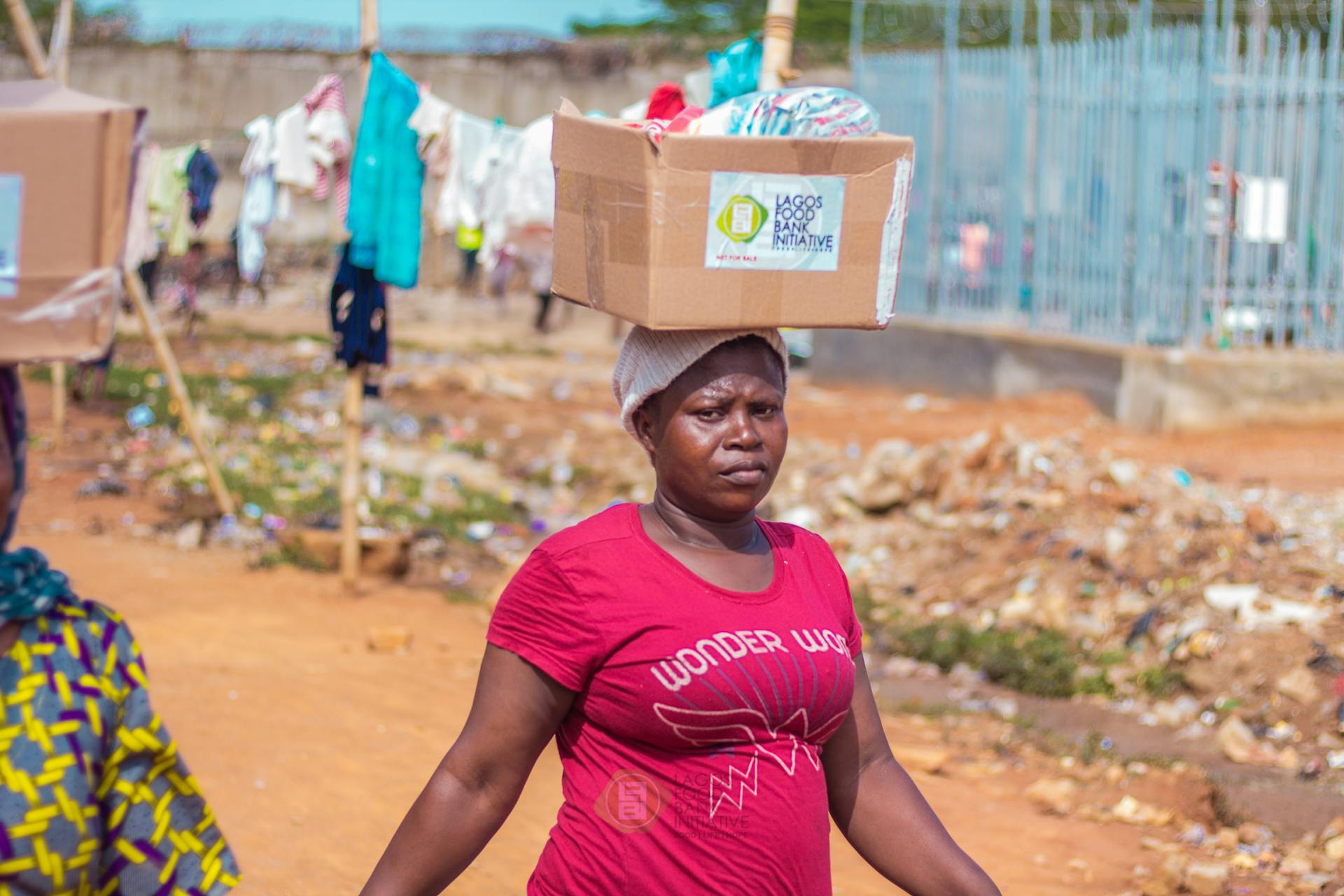 African woman in pink shirt carrying a donation box outdoors in Lagos, Nigeria.