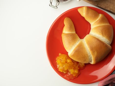 A tasty croissant served with apricot jam on a vibrant red plate, perfect for breakfast or snack.