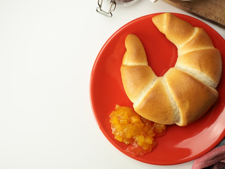 A Croissant And Apricot Jam On A Red Plate