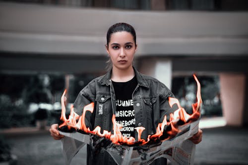 Shallow Focus Photo of Woman in Black Denim Jacket Holding a Burning Newspaper