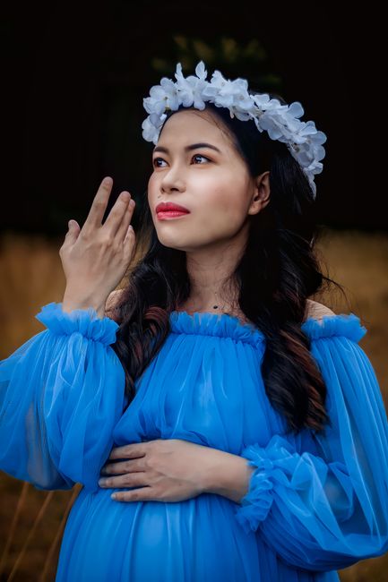 Thoughtful pregnant Asian woman with hairstyle in stylish blue dress looking away in nature in daytime
