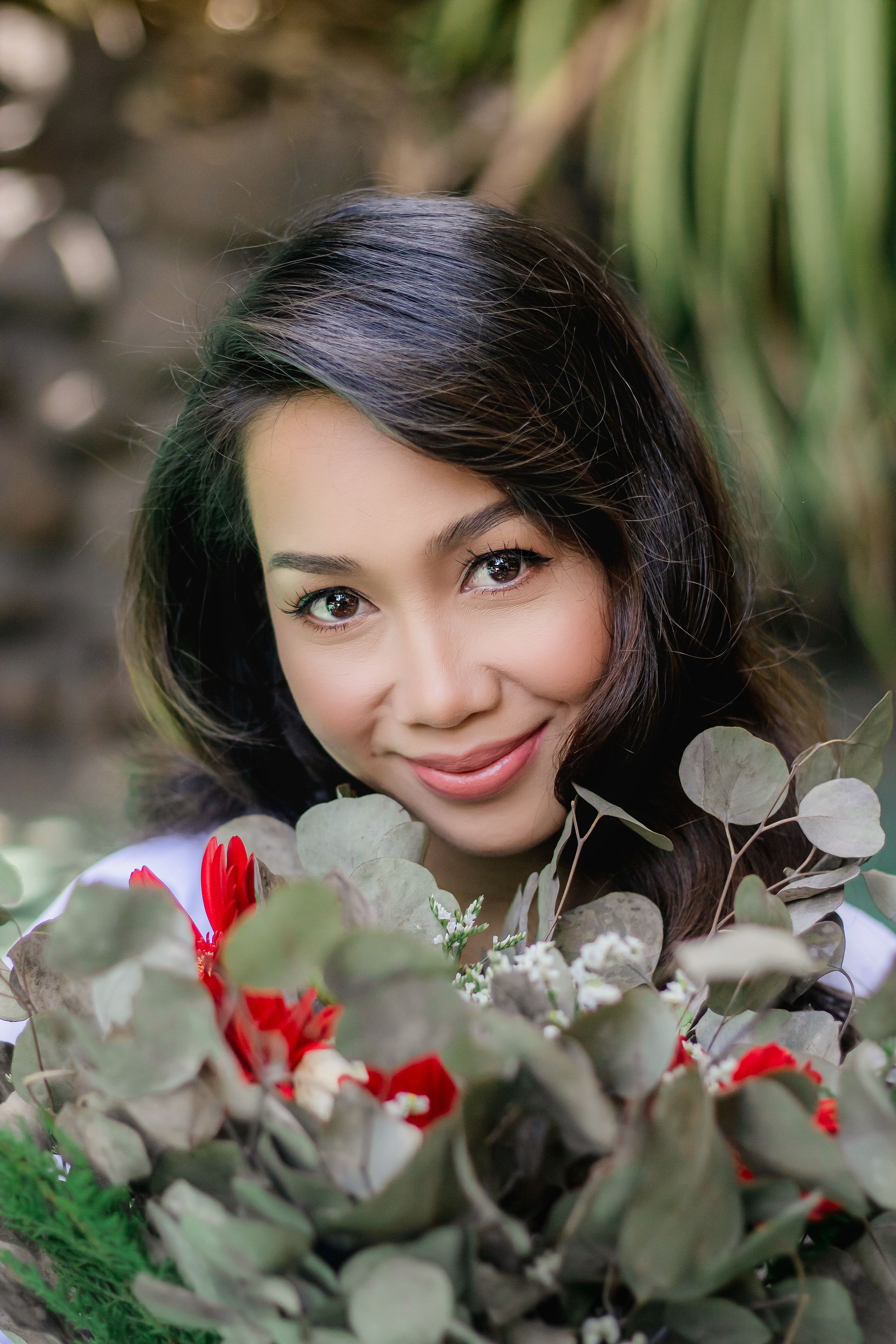 Smiling Asian woman with bouquet of flowers with eucalyptus looking at camera in nature in daylight