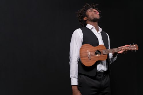 Free A passionate musician playing ukulele against a black backdrop, conveying emotion and artistry. Stock Photo
