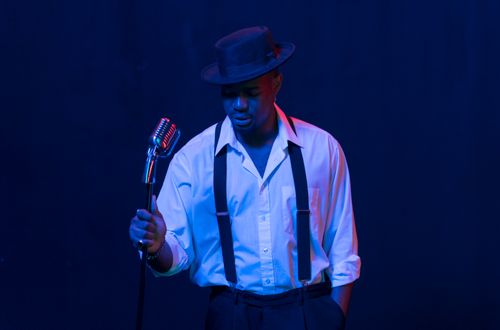 Free Stylish jazz singer in a hat performing under blue stage lights with a vintage microphone. Stock Photo