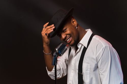 Free Smiling African American singer in a black hat and white shirt, performing with a vintage microphone. Stock Photo