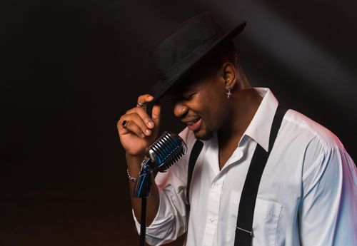 Free Black singer performing with a vintage microphone, exuding emotion and style on a dimly lit stage. Stock Photo