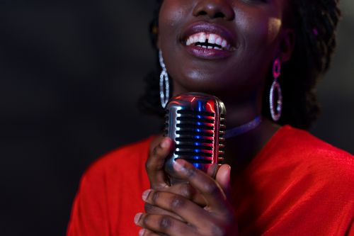 Free African American woman singing into a vintage microphone, highlighting expressive emotion and stage presence. Stock Photo