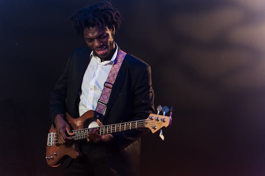 African American musician in a suit playing bass guitar on stage with vibrant lights.